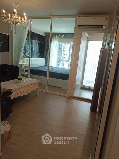 Modern living room with elegant chandelier and glass partition leading to a cozy bedroom.