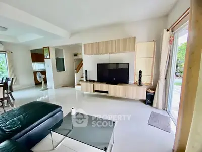 Spacious living room with modern decor and large TV, open to outdoor patio.