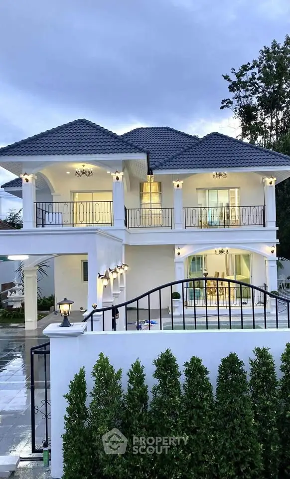 Stunning two-story white house with elegant balcony and lush greenery, perfect for luxurious living.