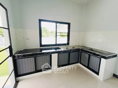 Modern kitchen with sleek black countertops and large window offering natural light.