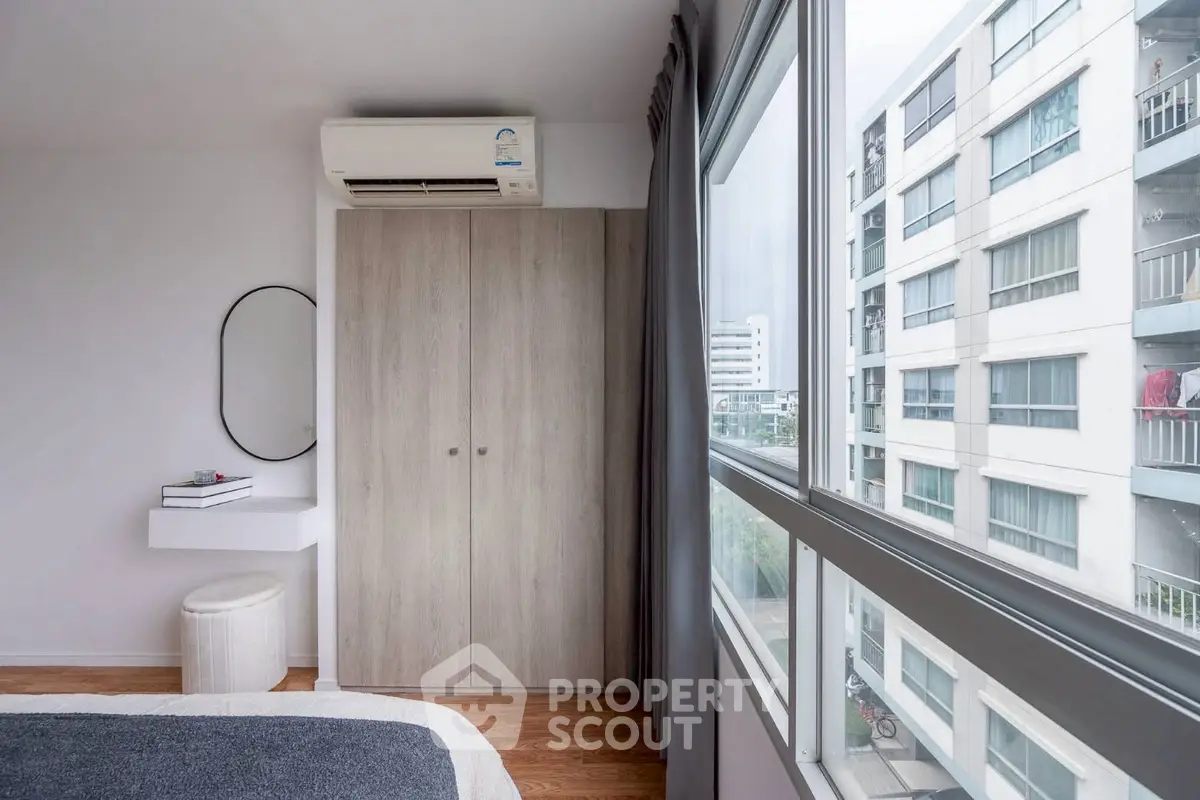 Modern bedroom with large window and built-in wardrobe in urban apartment