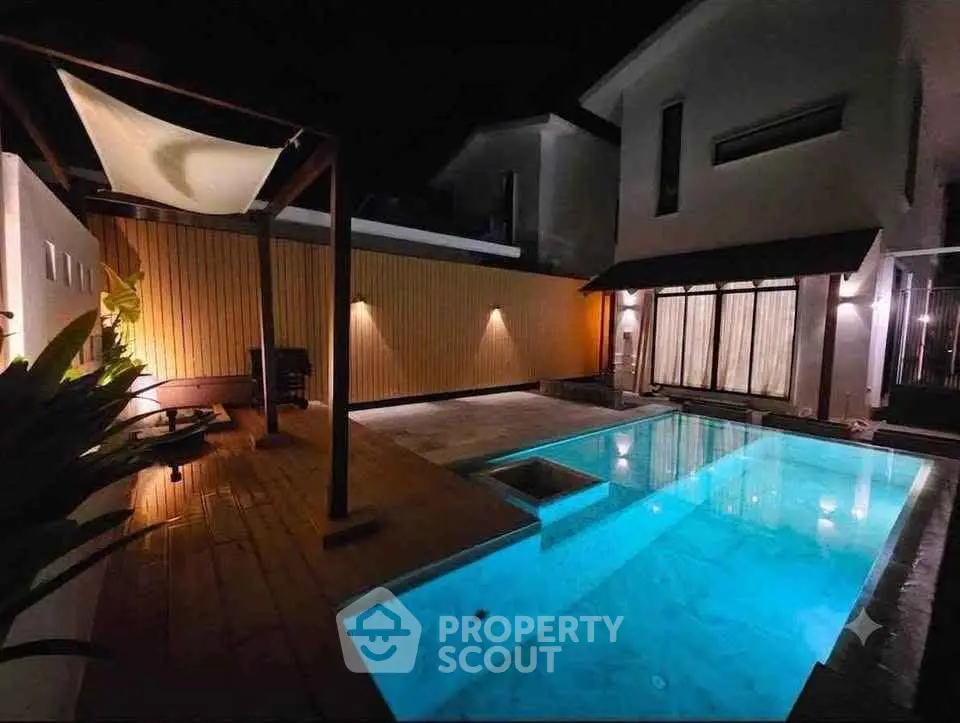 Luxurious modern home with illuminated pool and stylish outdoor seating area at night.