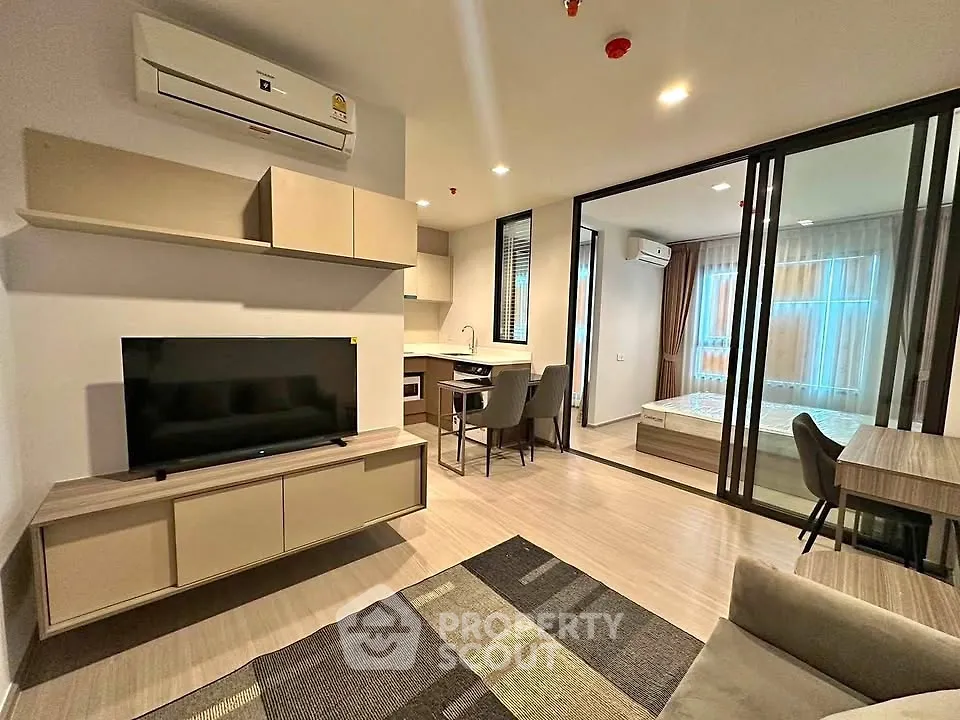 Modern open-plan living room with sleek furniture and glass partition to bedroom