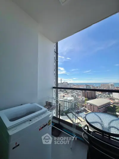 Stunning balcony view with cityscape and ocean, featuring a washing machine and seating area.