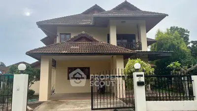 Charming two-story house with tiled roof and gated entrance, surrounded by lush greenery.