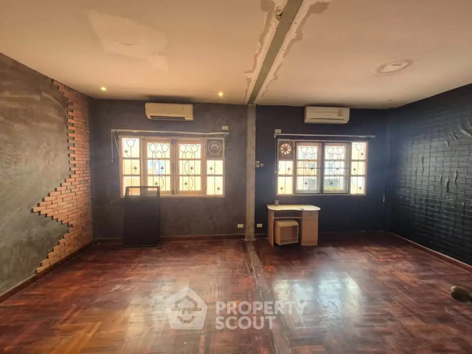 Spacious living room with unique brick and plaster wall design, featuring wooden flooring and large windows.