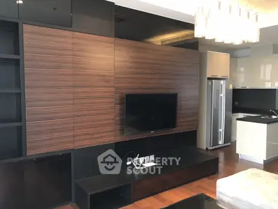Modern living room with sleek wooden paneling and open kitchen layout, featuring a flat-screen TV and contemporary lighting.