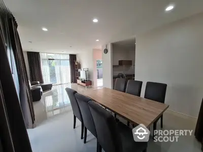 Spacious modern dining area seamlessly connected to a cozy living space, featuring a large wooden table, sleek black chairs, and ample natural light.