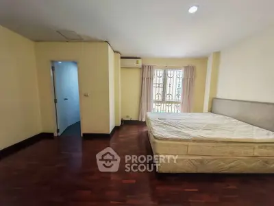 Spacious bedroom with wooden flooring and large window for natural light.