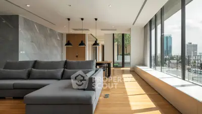 Spacious modern living room with large windows and city view, featuring sleek furniture and elegant lighting.