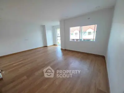 Spacious empty room with wooden flooring and large windows offering natural light.