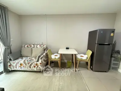 Cozy living area with floral sofa, dining table, and modern fridge in a bright apartment.