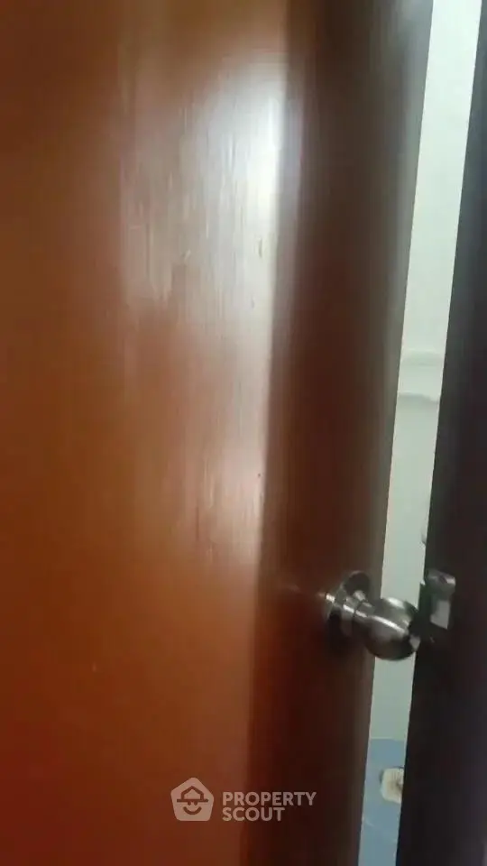 Partially open wooden door with metal handle leading to a tiled room.