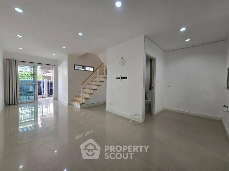 Spacious modern living room with staircase and large windows in a bright, open layout home.