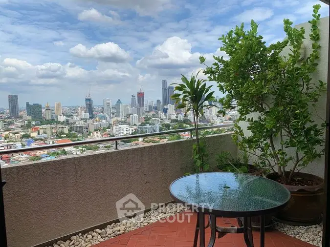 Spacious balcony with panoramic city views, featuring a glass-top table and lush potted plants, ideal for outdoor relaxation and urban living.