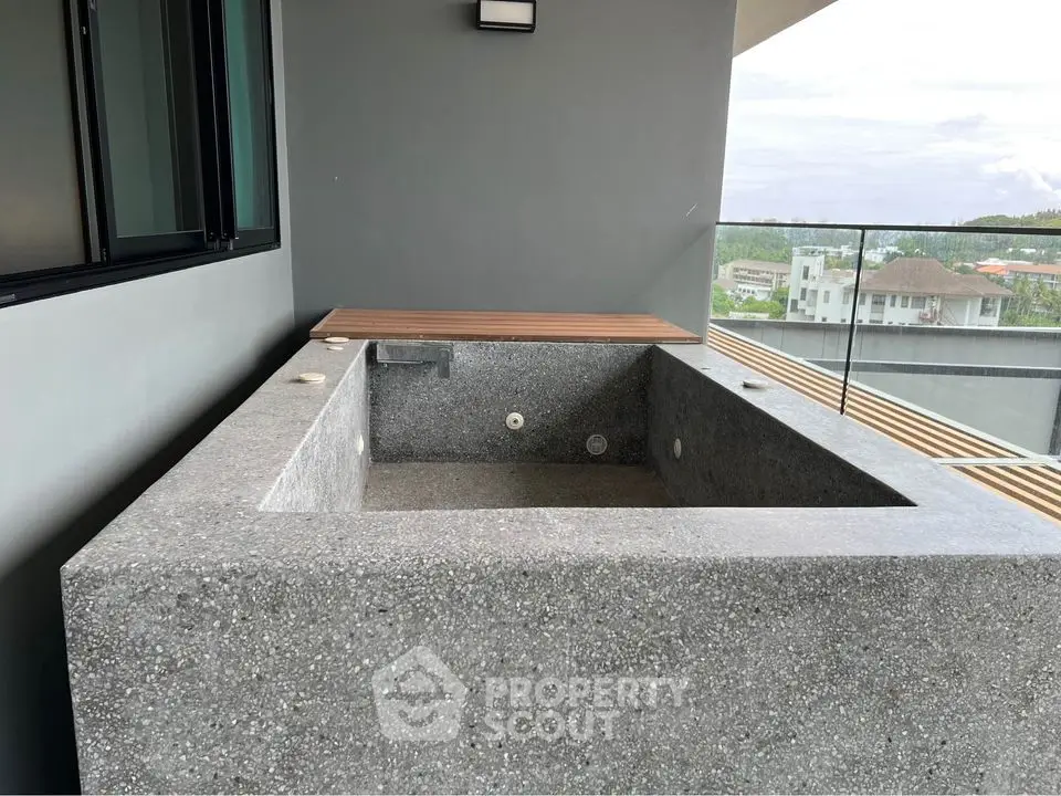 Modern balcony with concrete bathtub and glass railing offering scenic views.