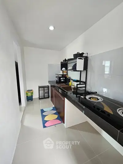 Modern kitchen with sleek black countertops and open shelving, featuring a gas stove and colorful rug.