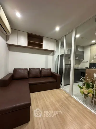 Modern living room with brown leather sofa and open kitchen layout in a cozy apartment.