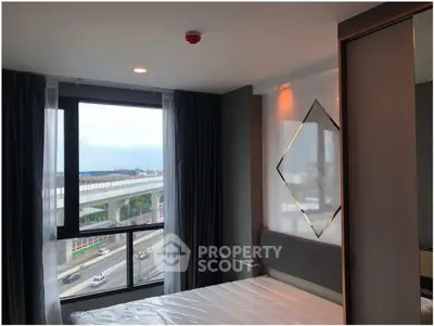 Modern bedroom with large window offering city view, stylish decor and ample natural light.