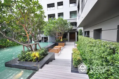 Luxurious apartment complex with serene garden and poolside seating area