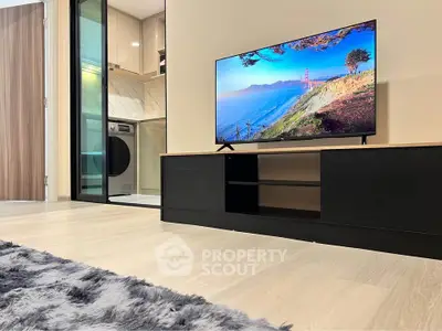 Modern living room with TV and view into sleek kitchen with washing machine.