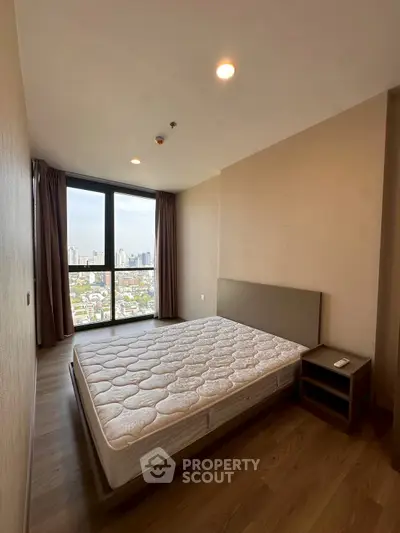 Spacious bedroom with large window offering stunning city views, featuring a comfortable bed and elegant wooden flooring.