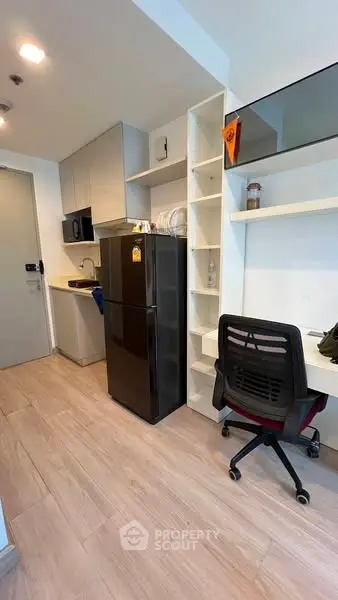 Modern compact kitchen with fridge and study area in a stylish apartment.