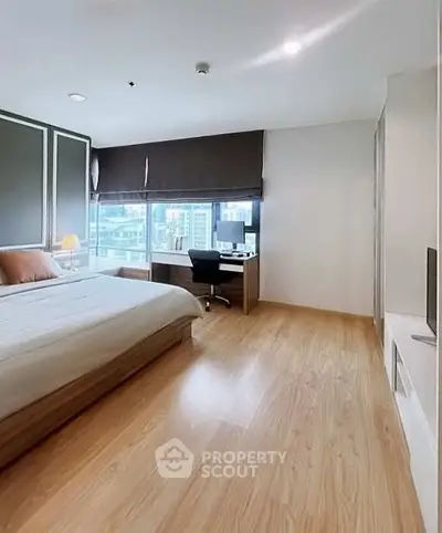 Spacious bedroom with modern decor and large window offering city views, featuring a cozy bed and work desk.