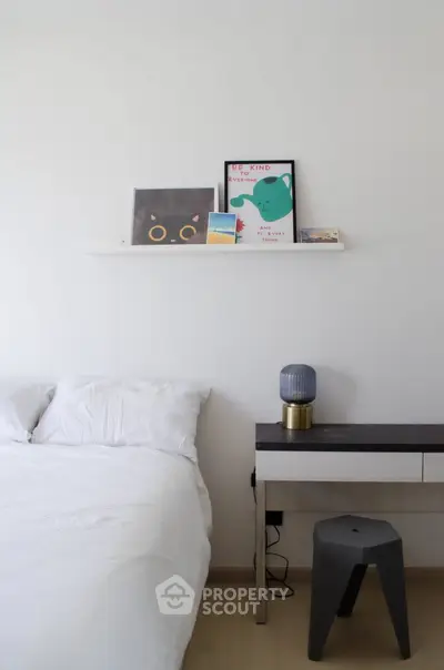 Modern minimalist bedroom with white bedding, wall art, and sleek bedside table with lamp.