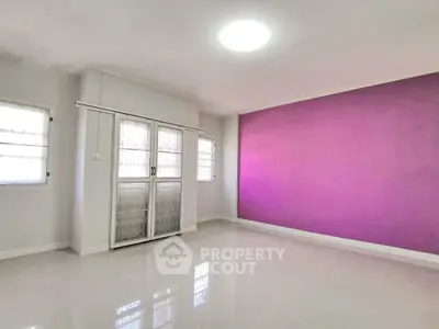 Spacious empty room with vibrant purple accent wall and white tile flooring