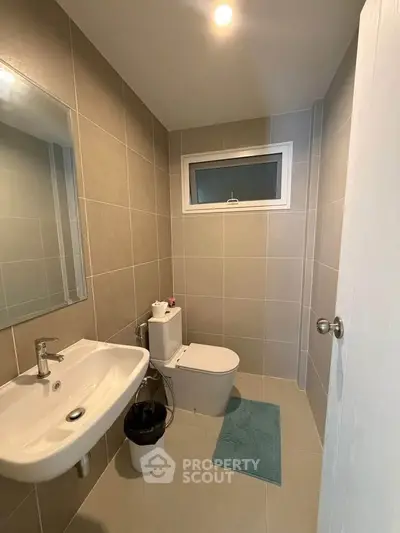 Modern bathroom with sleek fixtures and neutral tiles, featuring a window for natural light.