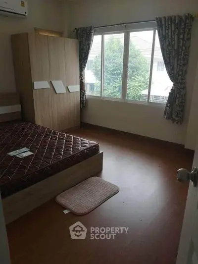 Cozy bedroom with large window and wooden flooring, featuring a spacious wardrobe and comfortable bed.