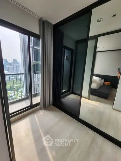 Modern bedroom with floor-to-ceiling windows and city view, featuring sleek mirrored closet doors.