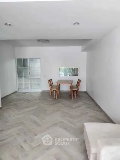 Spacious minimalist living room with wooden flooring and simple dining set.