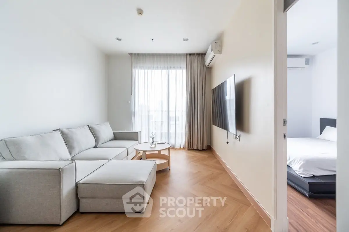 Modern living room with cozy sectional sofa and wall-mounted TV, adjacent to a bright bedroom.