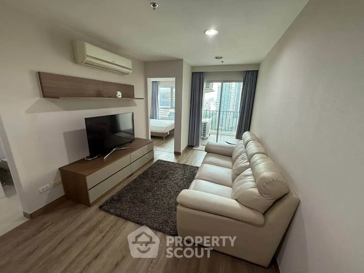Modern living room with leather sofa and TV, open view to bedroom and balcony.