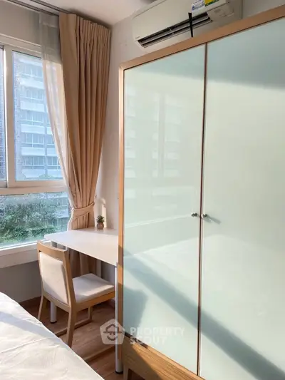 Cozy bedroom with natural light, featuring a wardrobe and study desk near a window.