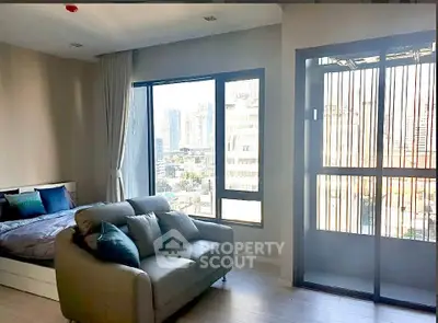 Modern studio apartment with city view, featuring a cozy bed and stylish sofa near large windows.