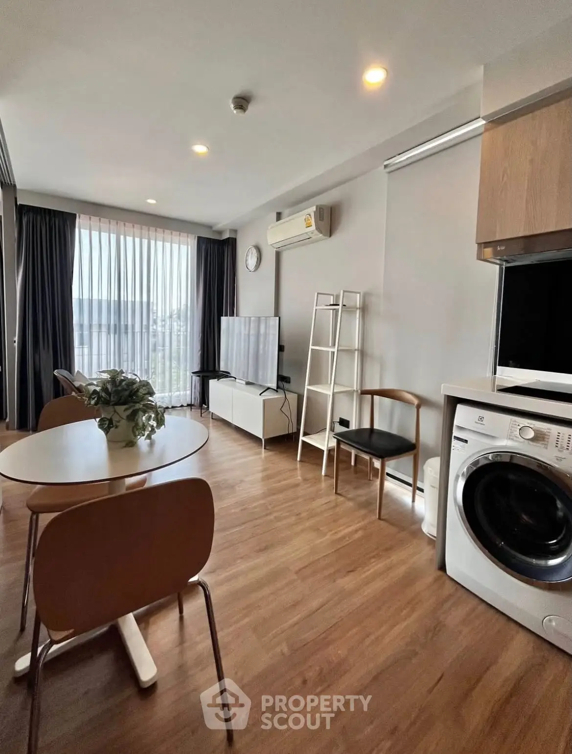 Modern living room with wooden flooring, dining area, and in-unit washing machine.