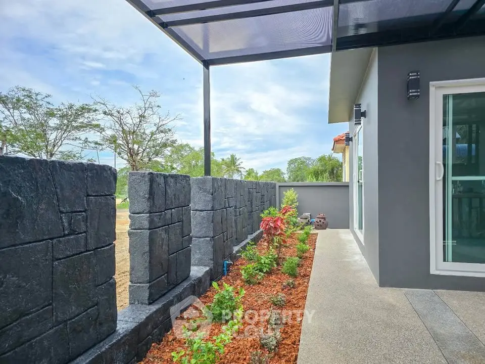 Modern home exterior with landscaped garden and stone wall under a sleek pergola.