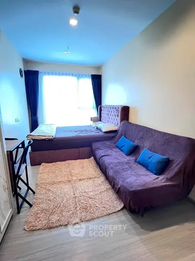 Cozy bedroom with stylish sofa and plush rug, featuring large window for natural light.