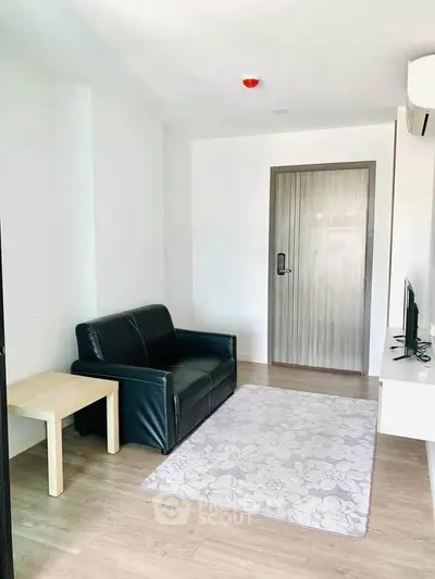 Modern living room with black leather sofa, wooden flooring, and minimalist decor.