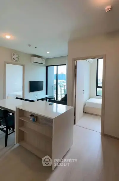 Modern apartment interior with open layout kitchen and cozy living area, featuring large windows and natural light.