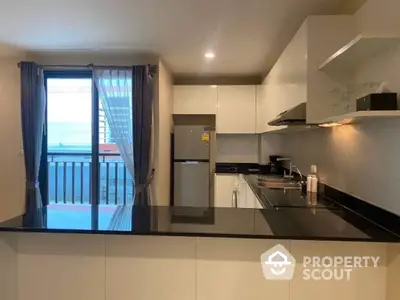 Modern kitchen with sleek black countertops, stainless steel appliances, and a view of the balcony offering natural light and outdoor access.