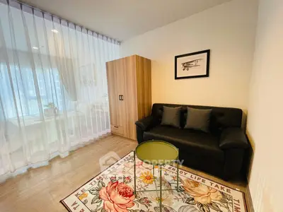 Cozy living room with modern sofa, floral rug, and natural light through sheer curtains.