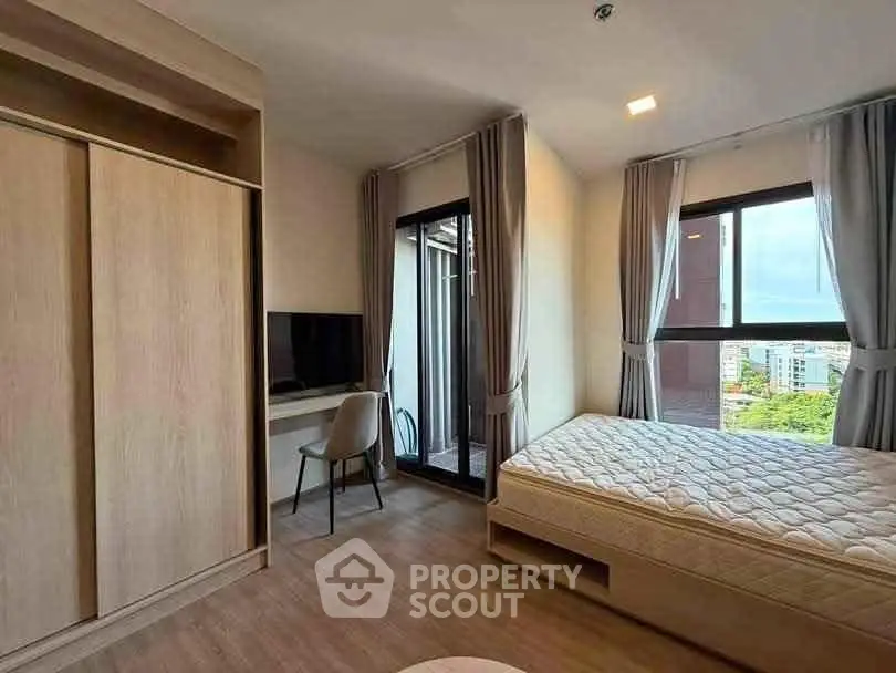 Modern bedroom with balcony access and city view, featuring built-in wardrobe and sleek desk area.