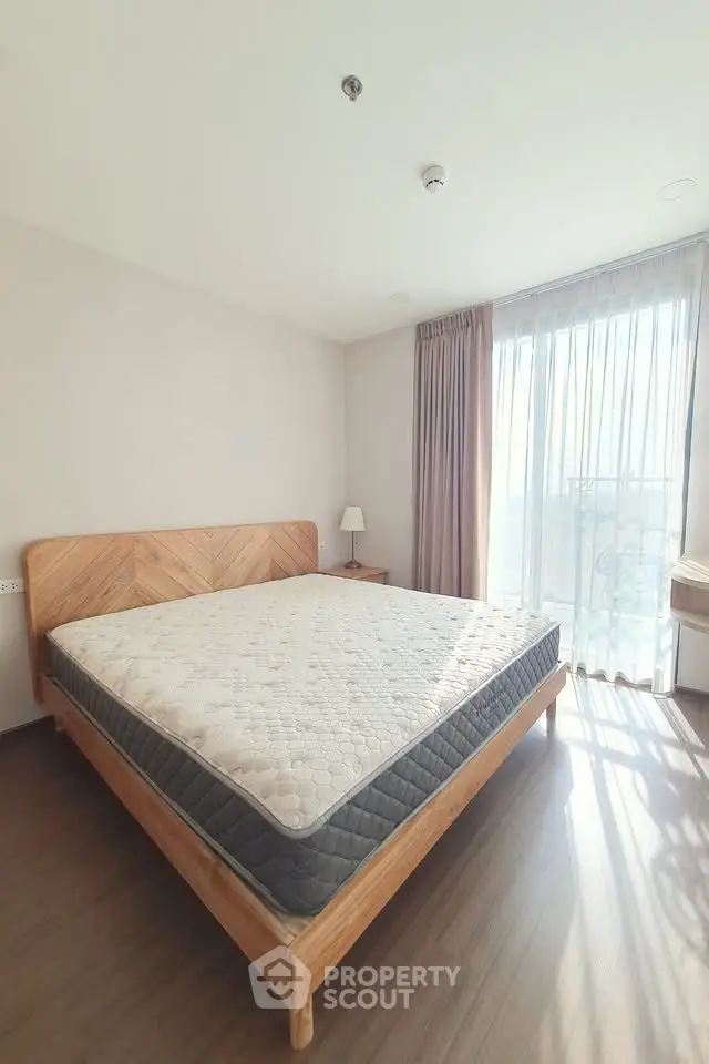 Bright and airy bedroom with wooden bed frame and large window view.