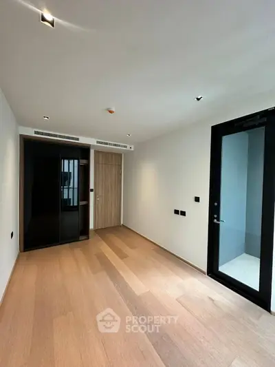 Spacious modern bedroom with wooden flooring and sleek black wardrobe