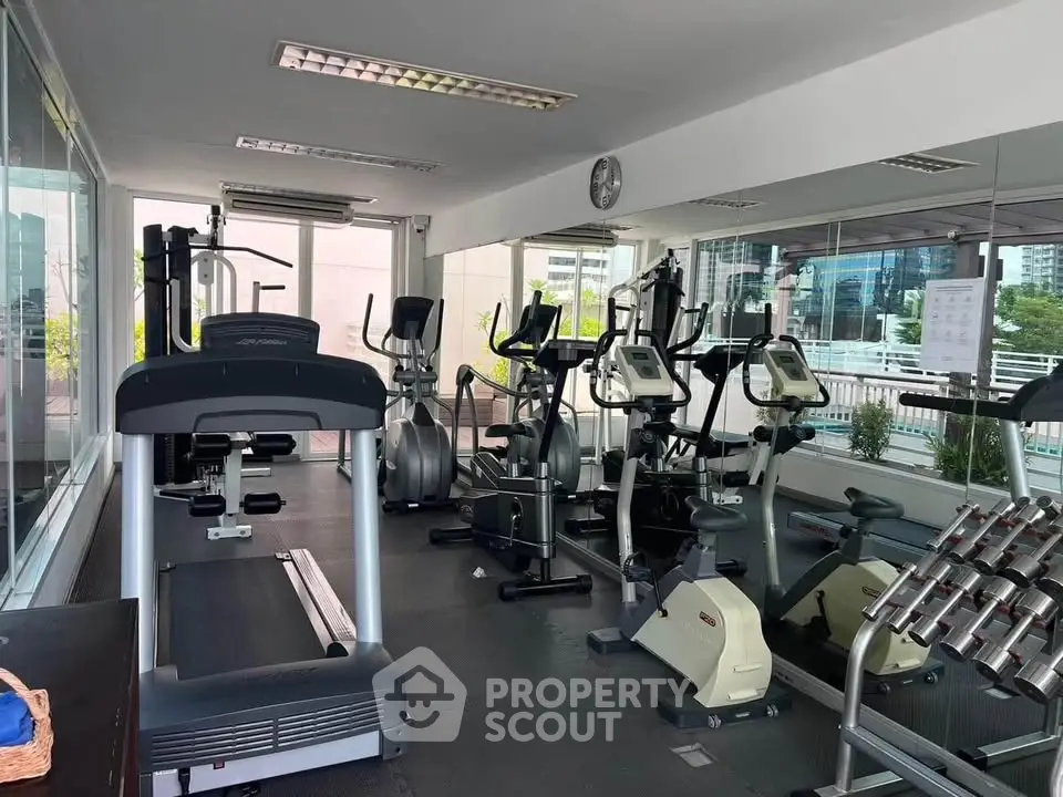 Modern gym with cardio equipment and weights in a bright, glass-walled space.