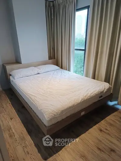 Cozy bedroom with large window and wooden flooring, offering a serene view of the cityscape.